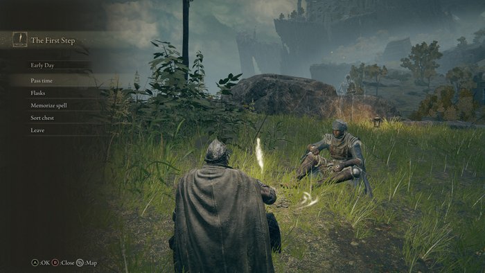 Dwójka graczy w grze Elden Ring siedzi przy ognisku na trawie. Ubrani są w hełmy i prosty oręż. W tle zamglone wzgórza.
