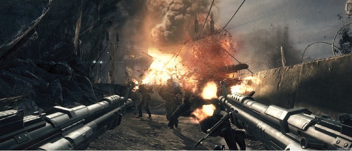 Opisujemy: widzimy obrazek z gry Wolfenstein: The New Order. Na pierwszym planie dwa symetrycznie trzymane karabiny. W tle naziści, których zabijamy, oraz wybuchy. Jeszcze dalej widać ścianę z drutem kolczastym i dużo dymu. Obraz utrzymany w szarych barwach.