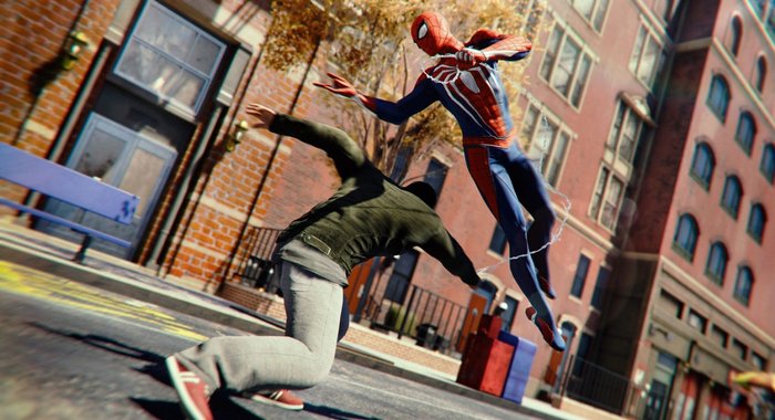 Opisujemy: screenshot z Marvel's Spider-Man Remastered. Postać ubrana w robocze ubrania próbuje uderzyć Spider-Mana, który uskakuje w powietrze, trzymając w ręce swoją pajęczynę. W tle nowojorskie budynki z czerwonych cegieł; akcja dzieje się na ulicy.