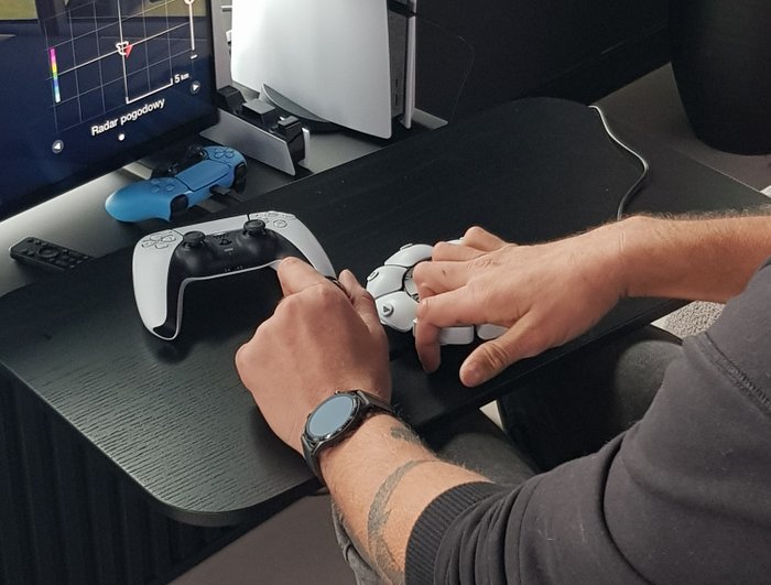 Zdjęcie przedstawia Piotra grającego na PlayStation Access w Gran Turismo. Zbliżenie na dłonie. Lewa trzyma gałkę, prawa naciska przyciski.